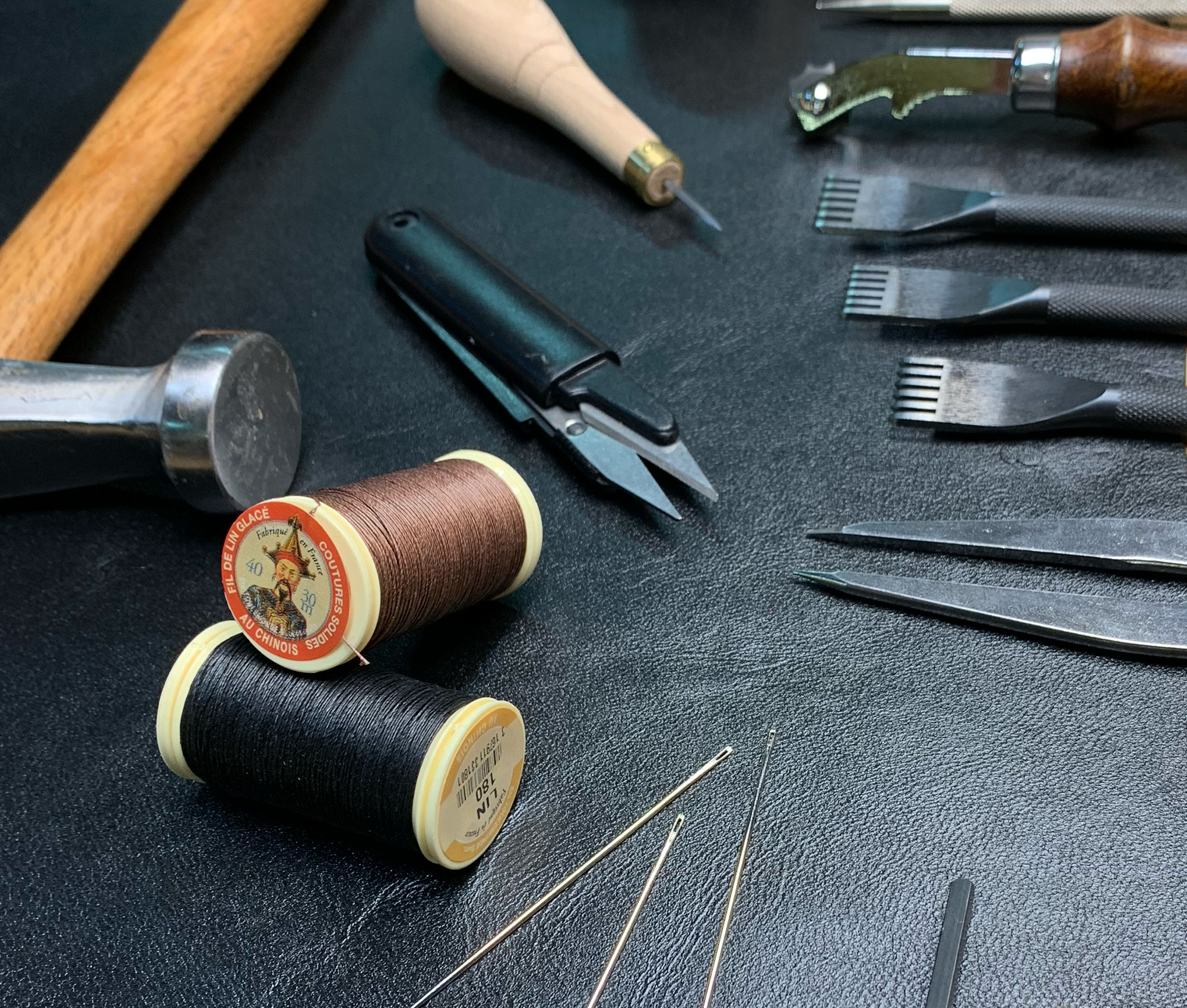 tous les outils utiles à la couture point sellier disposés sur un cuir noir